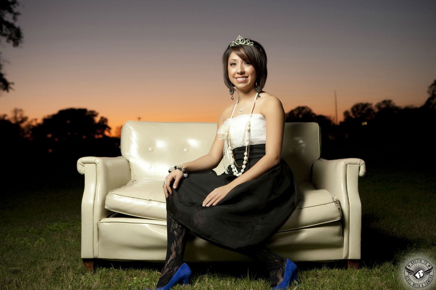 Picture of homecoming queen in fancy dress with blue high heels on couch in field with gorgeous sunset taken by Austin senior portrait photographer.